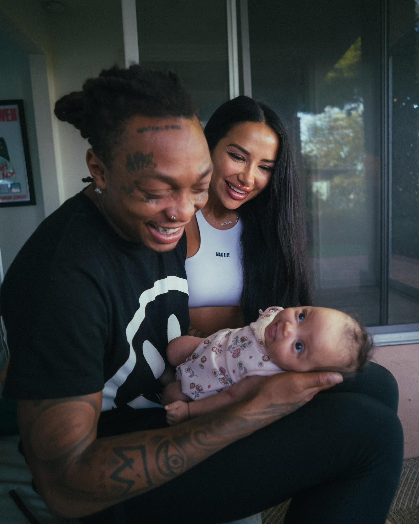 Music Artist Tyla Yaweh holding his daughter. His child's mother is also
 looking at the daughter. They are both smiling.